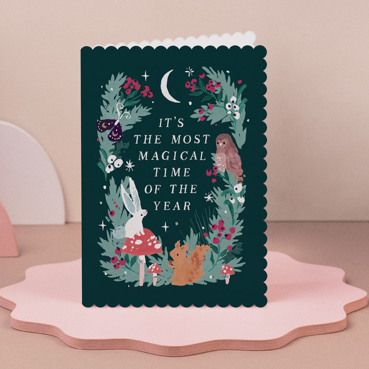 Christmas card with forest-themed illustrations and text on a pink stand.