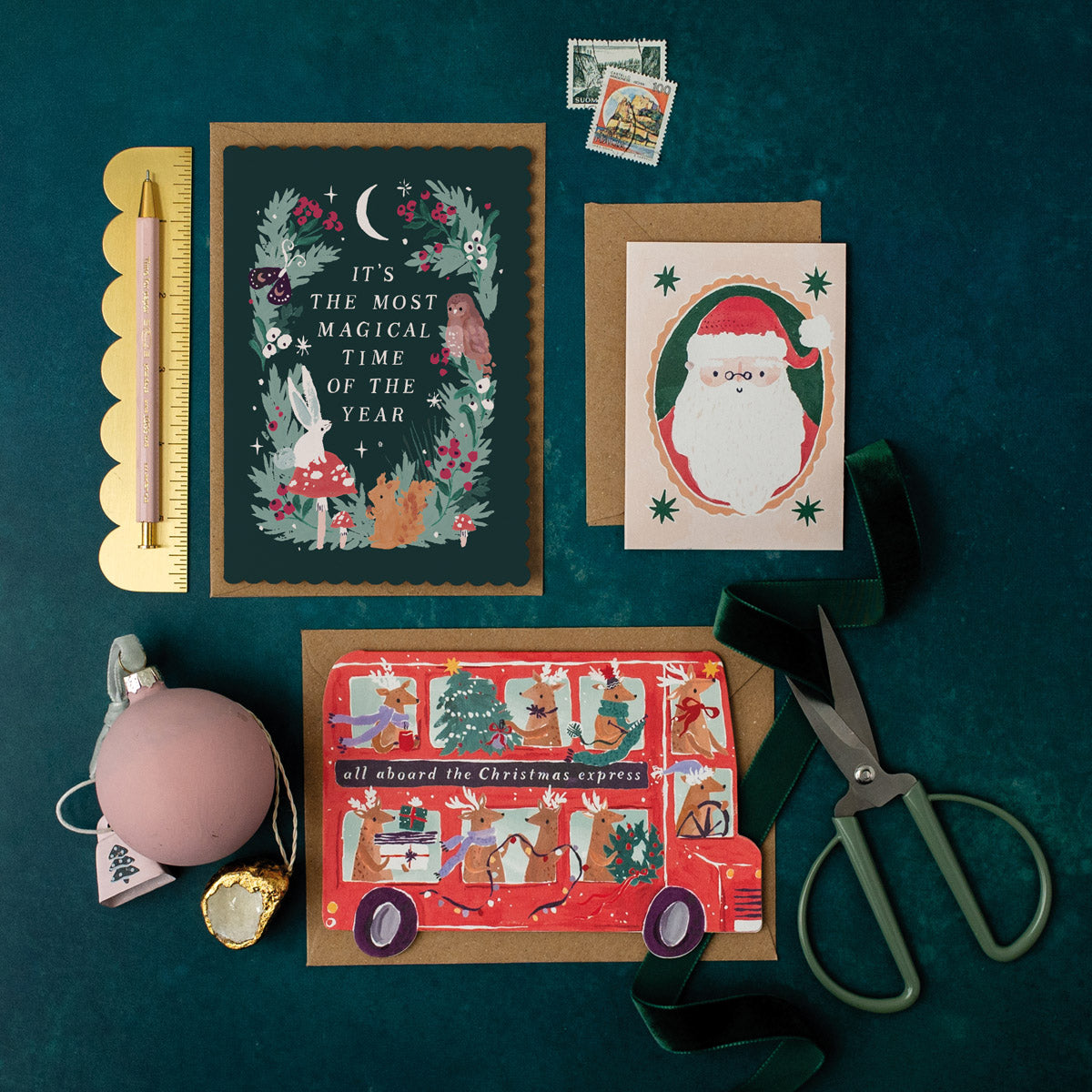 Collection of Christmas cards and decorations on a dark green surface with scissors and other items.