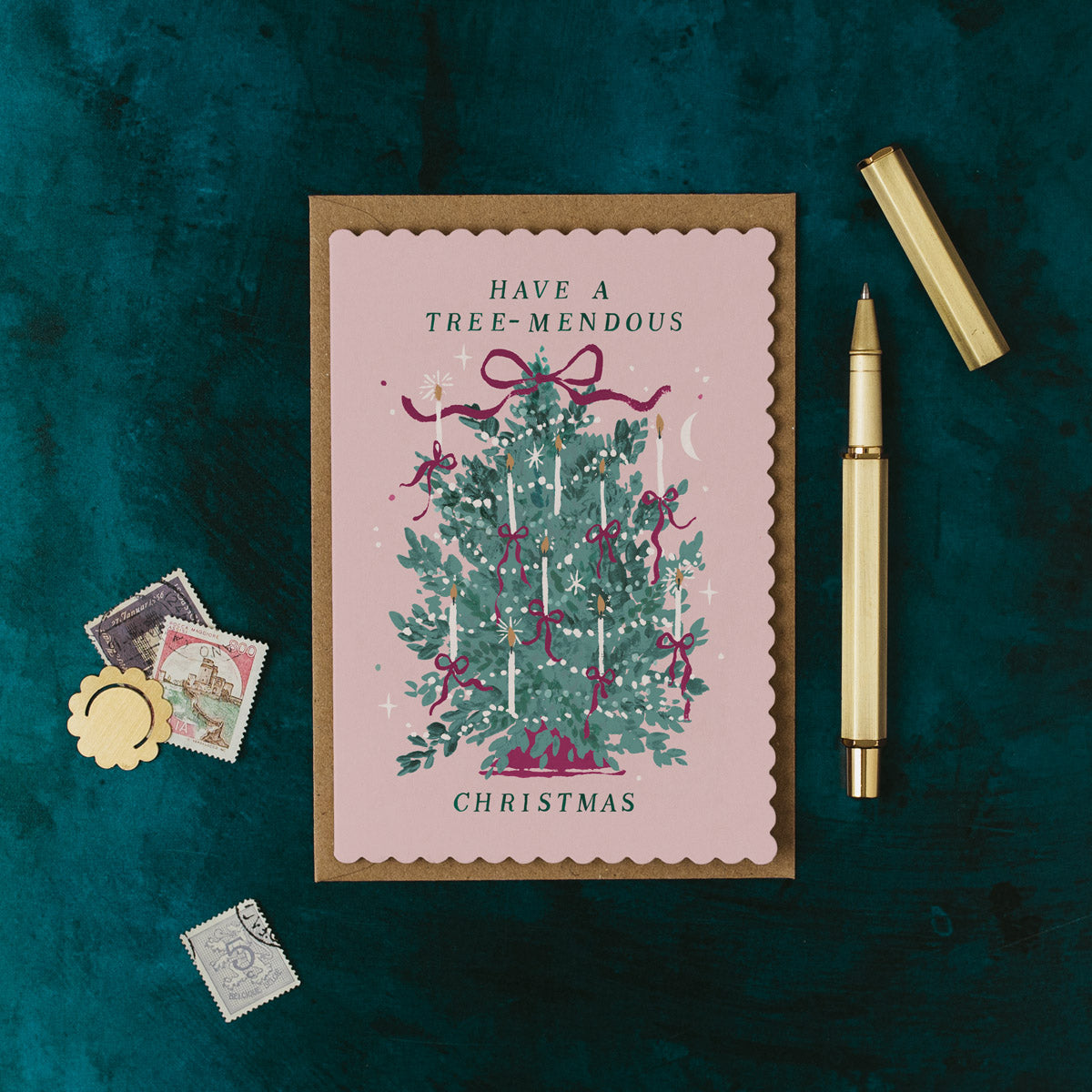 Christmas card with decorative tree and text on a dark green background with stationery items.
