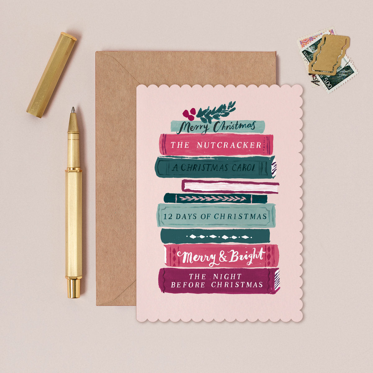Christmas-themed books stack Christmas card with envelope, pen, and stamps on a beige background