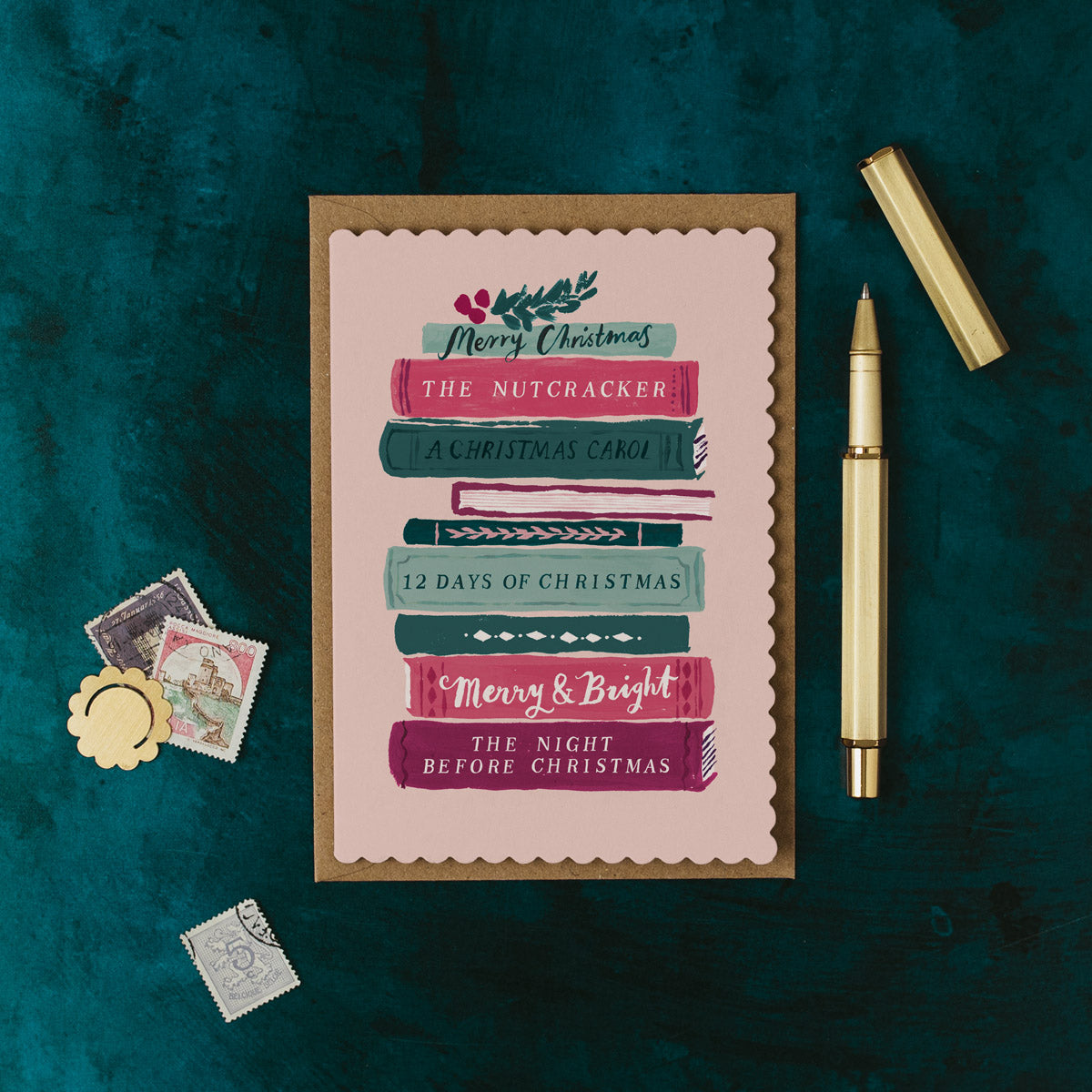 Christmas book stack greeting card on a dark green background with a pen and decorative items.