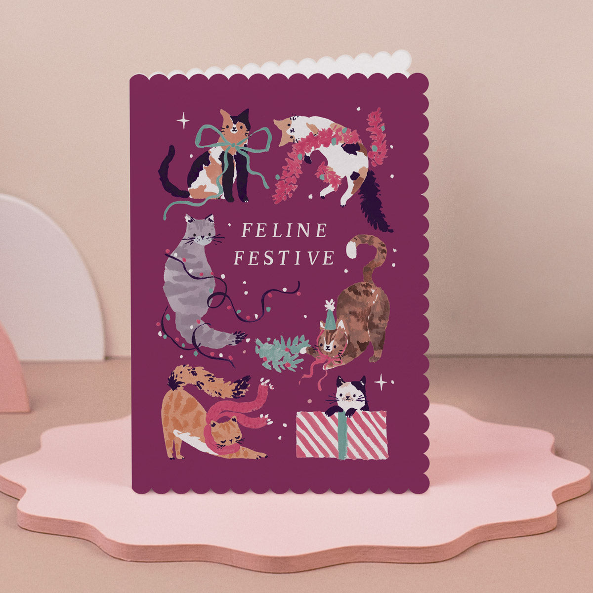 Christmas card with cat illustrations and 'Feline Festive' text on a pink stand.