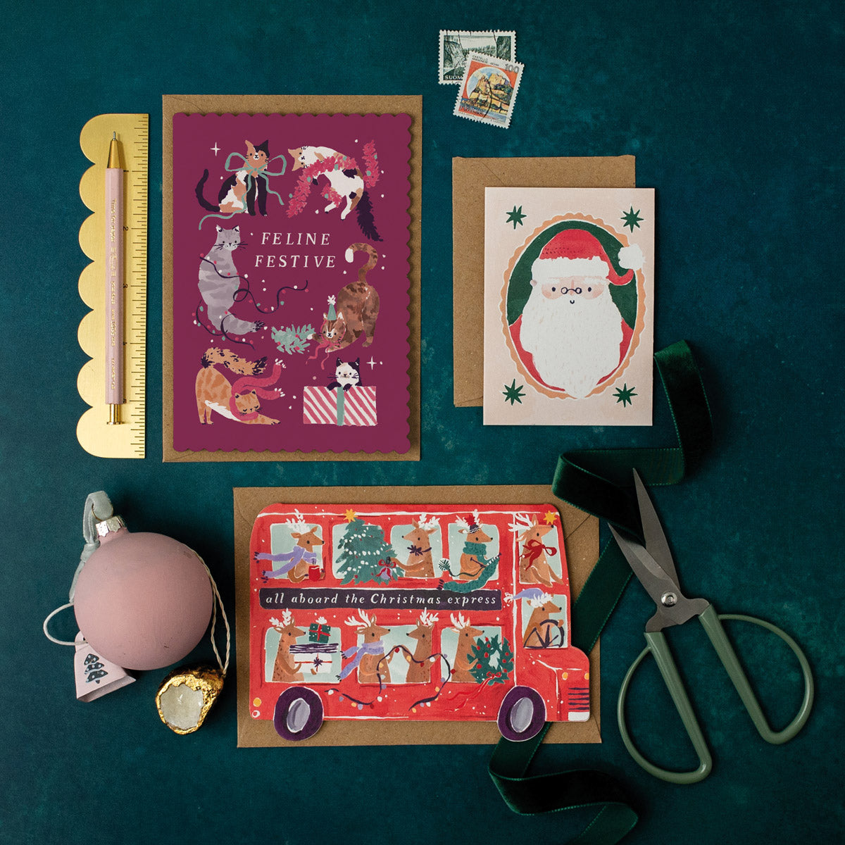 Cats Christmas greeting cards on a dark green surface with stationery items.