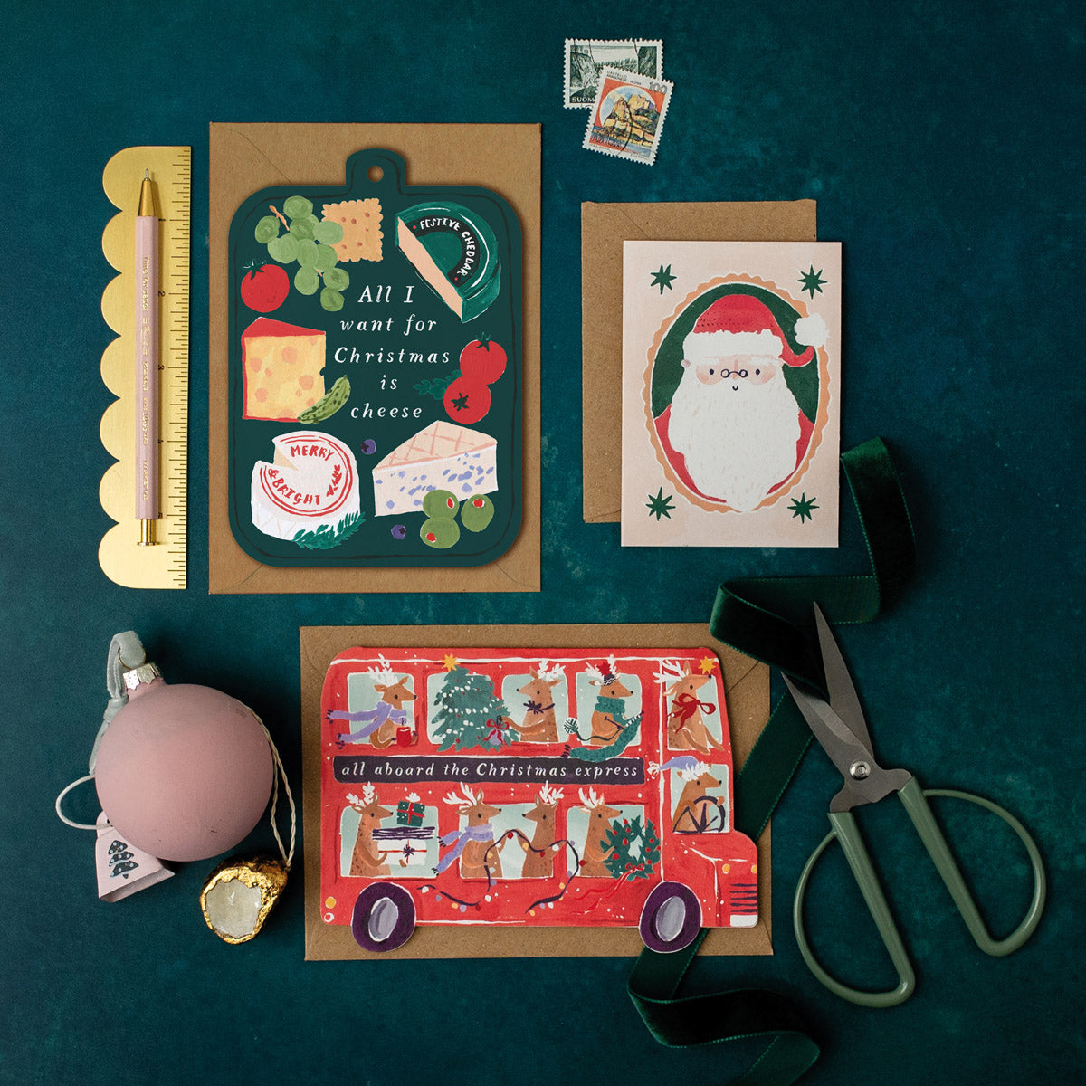 Collection of Christmas cards and stationery items on a dark green background including a cheese board cheese Holiday card.