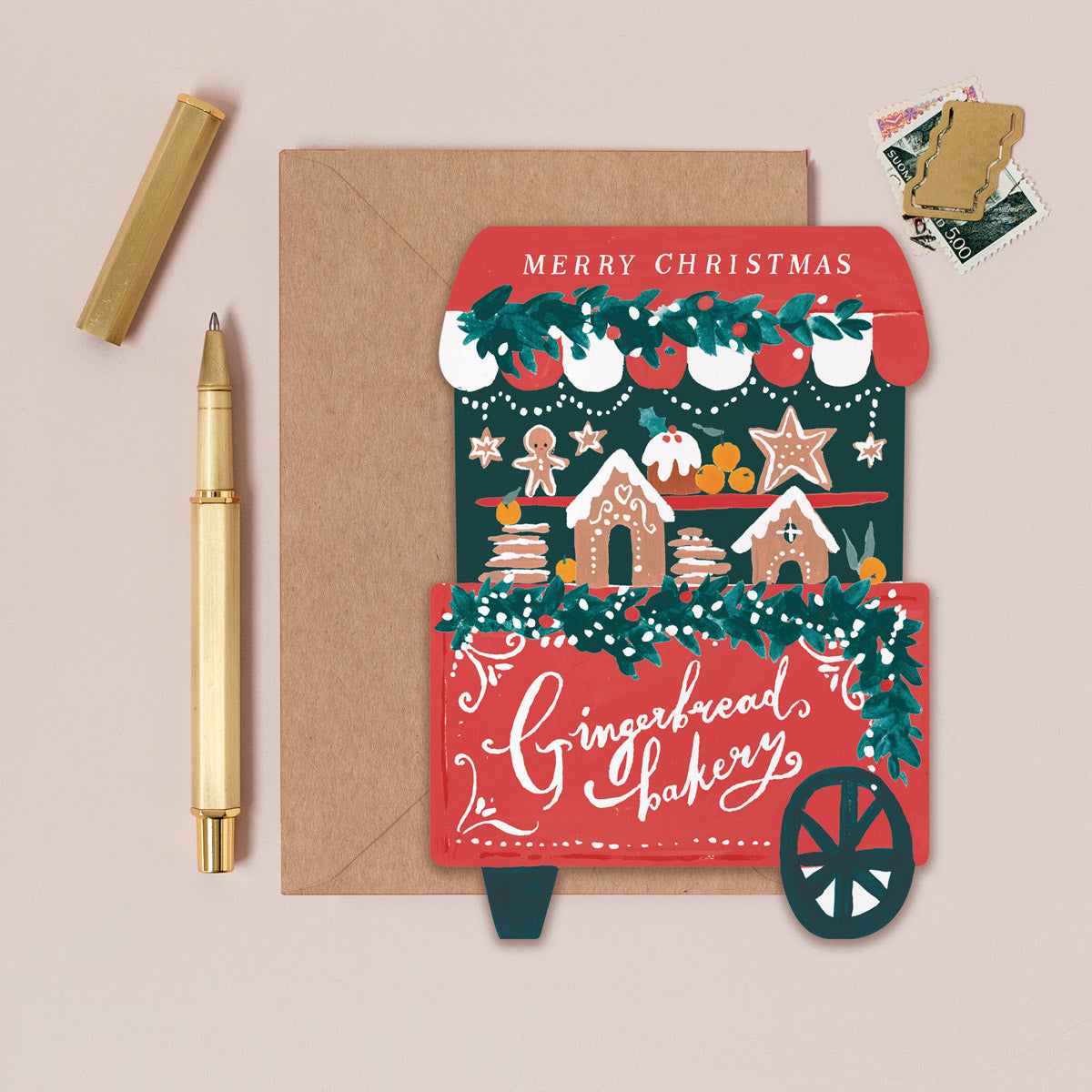 Christmas card with gingerbread bakery design, envelope, and pen on a beige background