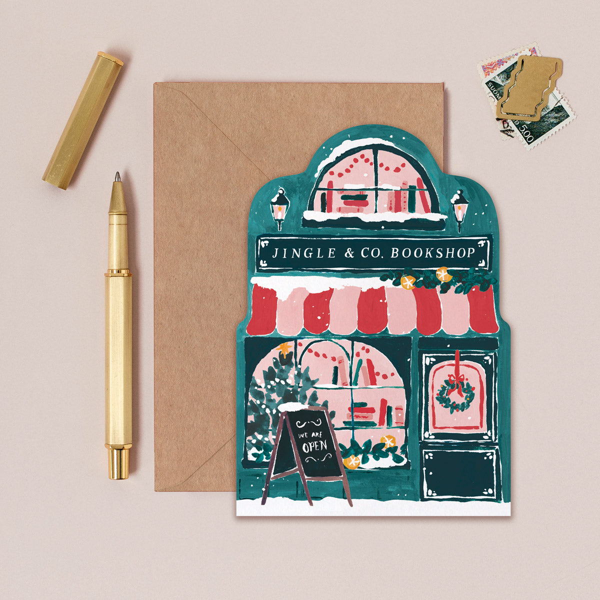 Bookish Christmas card with a festive bookshop illustration, envelope, pen, and stickers on a beige background