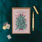 Christmas card with decorative tree and text on a dark green background with stationery items.