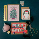 Three Christmas cards on a dark green surface with decorative items.
