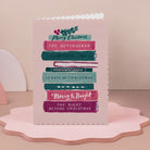 Bookish Christmas card, the Christmas book stack design appeals to those that love BookTok, it's on a pink scalloped edge stand.