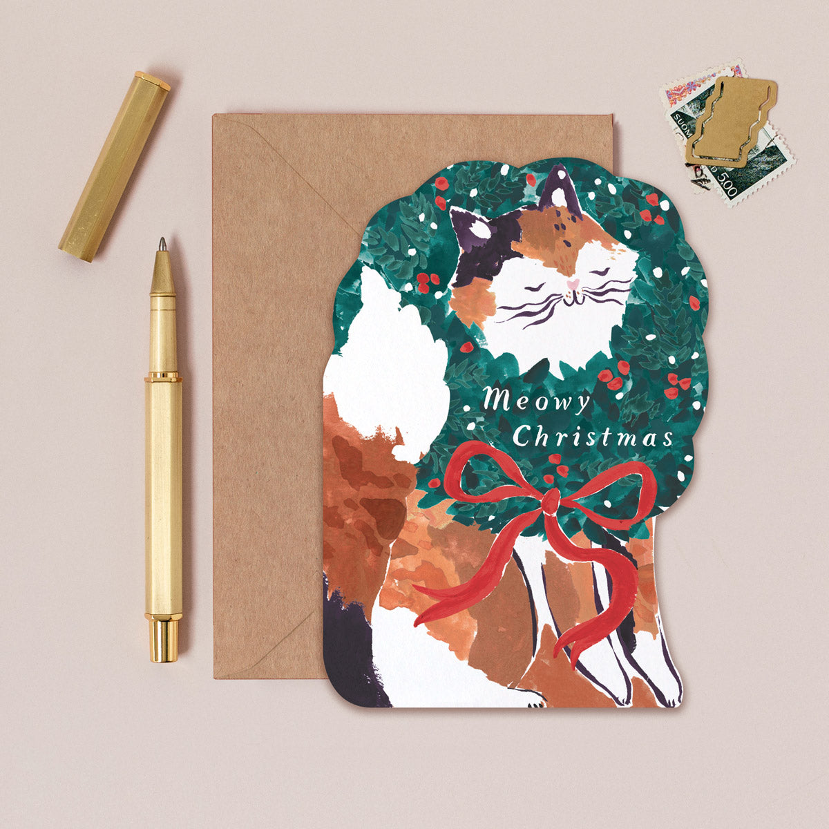 A Christmas card cut into the shape of a cat poking it's little face through a wreath from the wholesale Christmas card collection at Sister Paper Co.