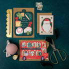 Collection of Christmas cards and stationery items on a dark green background including a cheese board cheese Holiday card.