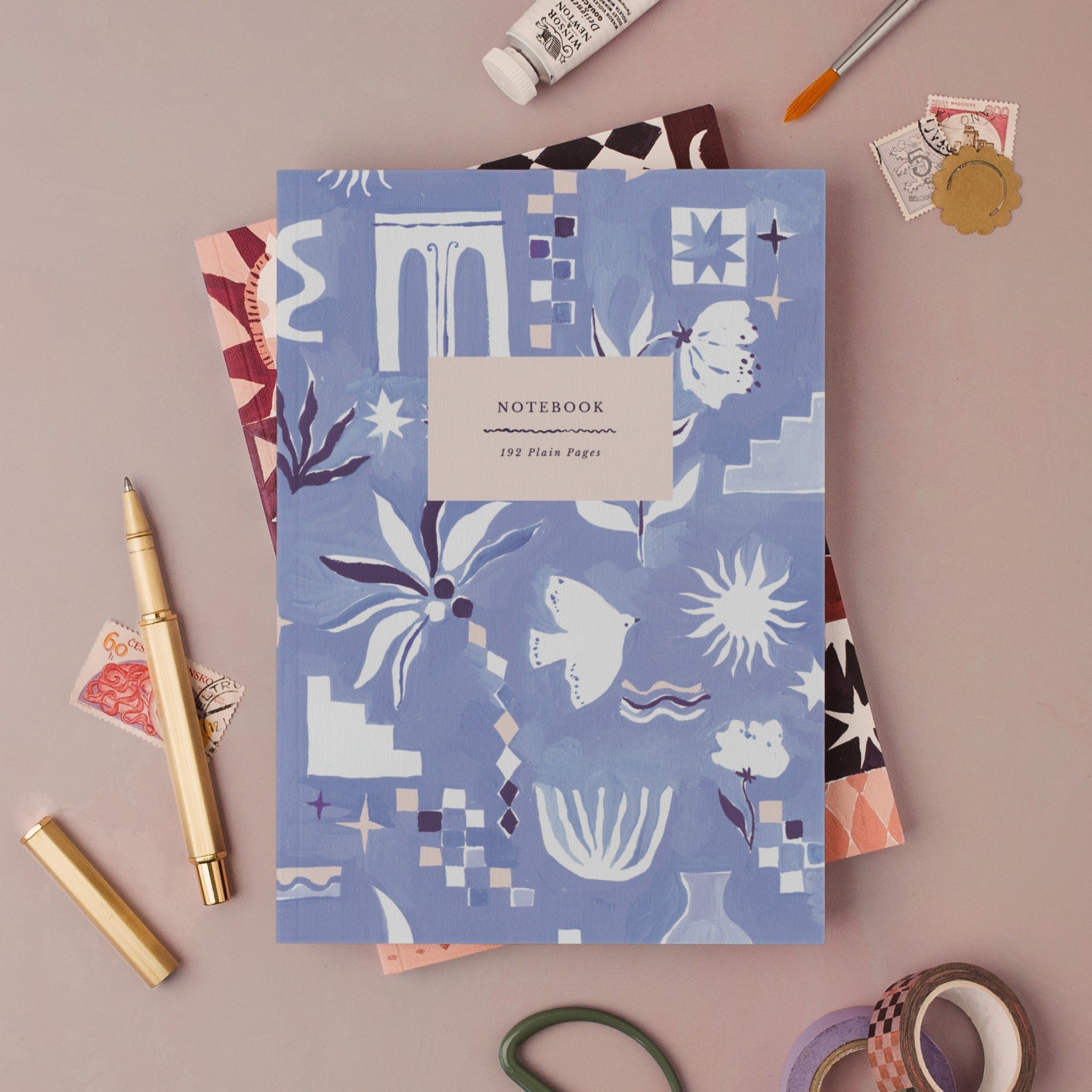 Medina Blue notebook, A5 plain page journal styled in a flat lay with a gold pen, paints and vintage stamps