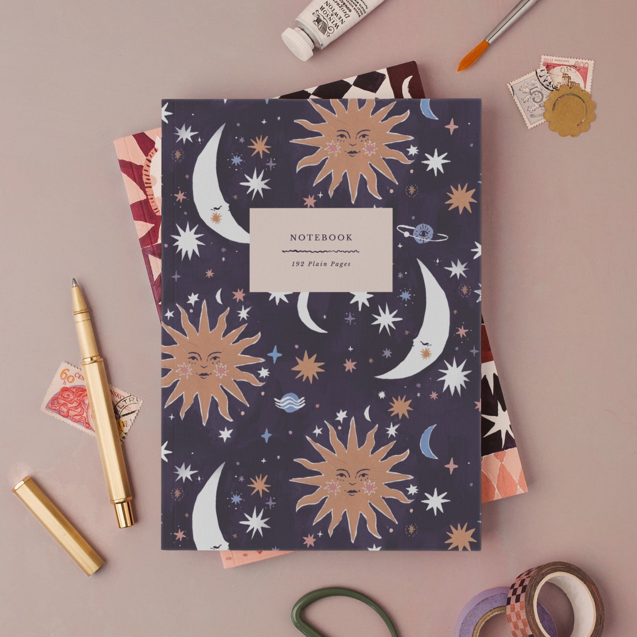 Sun and Moon notebook, A5 plain page journal styled in a flat lay with a gold pen, paints and vintage stamps