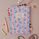 Cherries notebook, A5 plain page journal styled in a flat lay with a gold pen, paints and vintage stamps