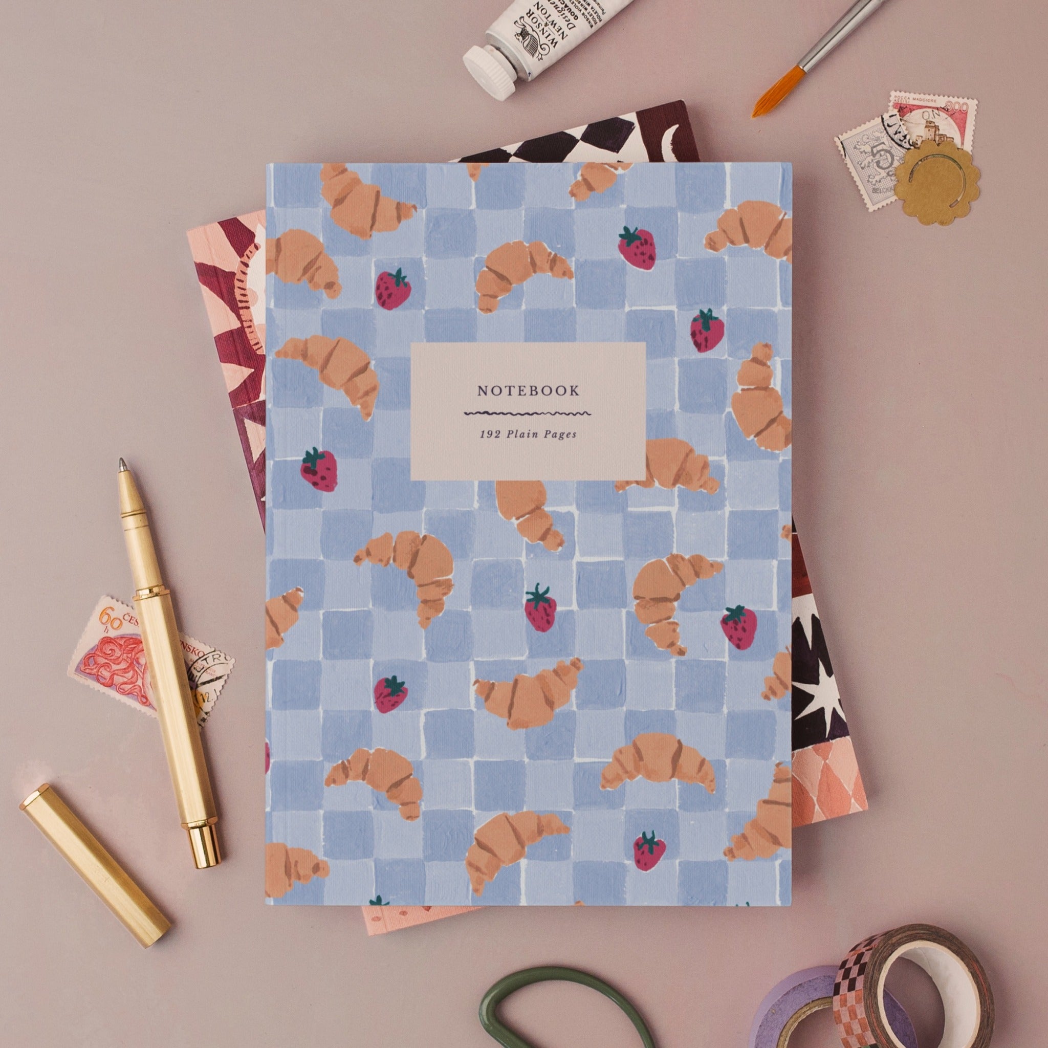Croissant Cafe notebook, A5 plain page journal styled in a flat lay with a gold pen, paints and vintage stamps