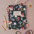 Mushrooms notebook, A5 plain page journal styled in a flat lay with a gold pen, paints and vintage stamps